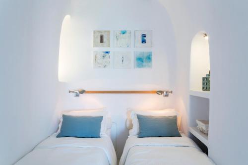 two beds in a room with white walls and blue pillows at Helestia Hotel, Caldera Santorini in Firostefani