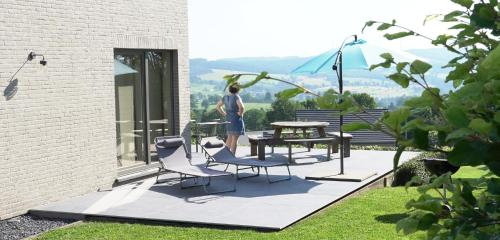a man standing on a patio with a table and chairs at "Petite perle en Haute Ardenne" avec vue sur la vallée, cabine infra-rouge et bain balnéo in Lierneux