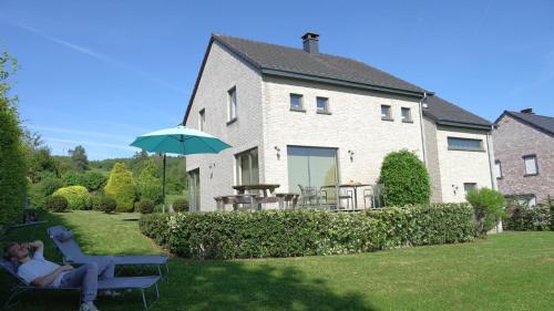 a woman sitting on a chair under an umbrella in front of a house at "Petite perle en Haute Ardenne" avec vue sur la vallée, cabine infra-rouge et bain balnéo in Lierneux