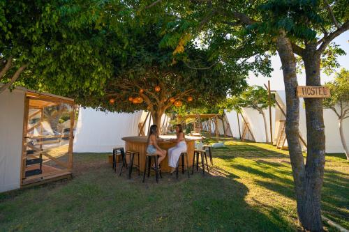 two women sitting at a table under a tree at Kampaoh Hostel Trafalgar in Los Caños de Meca