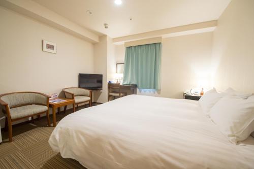 ein Hotelzimmer mit einem großen weißen Bett und Stühlen in der Unterkunft Shizunai Eclipse Hotel in Shinhidaka