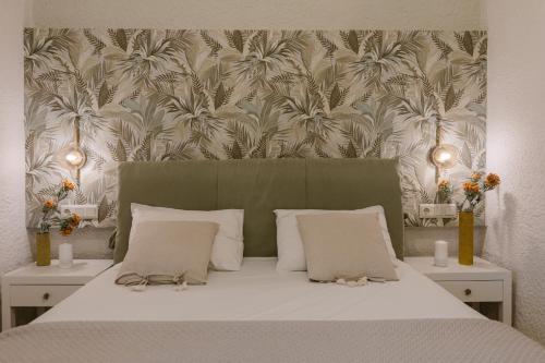 a bedroom with a bed with white sheets and a wallpaper with palm trees at Perla Apartments in Agia Pelagia