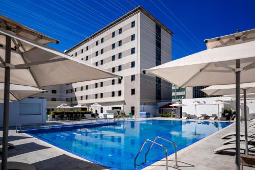 a swimming pool with white umbrellas and a building at Rénéa Hotel in Sétif