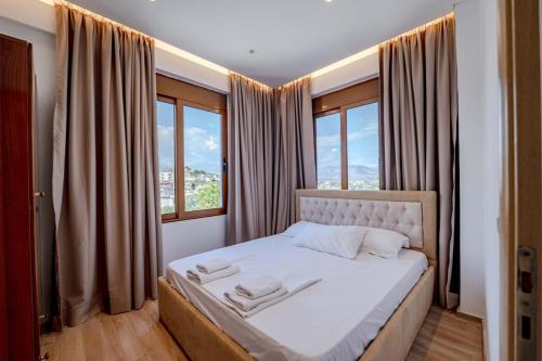 a bedroom with a bed with white sheets and windows at Villa HENA in Sarandë
