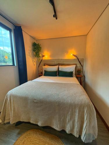 a bedroom with a bed with two pillows and a window at Tiny House Passaúna - Climatizado, parque e deck in Curitiba