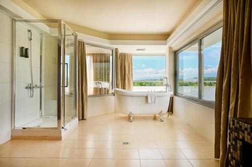 ein Badezimmer mit Badewanne und Dusche sowie Fenstern in der Unterkunft Cronwell Platamon Resort All-Inclusive in Platamonas