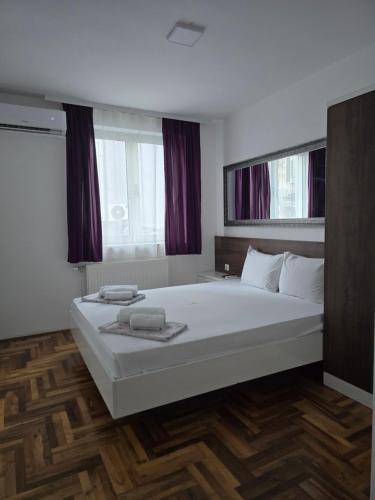 a bedroom with a large white bed with two windows at Sunny apartment in Niš
