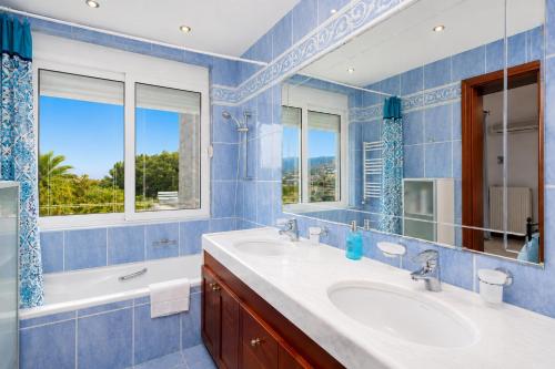 a blue bathroom with two sinks and a tub and windows at Villa Glan Y Mor in Elounda