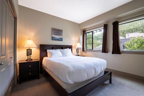 a bedroom with a large bed and two windows at Selkirk Snug by Revelstoke Vacations in Revelstoke