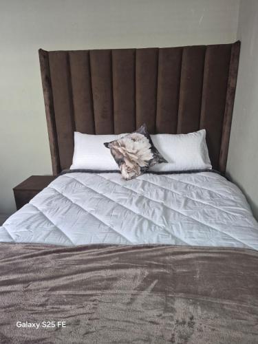 a bed with a brown headboard and white pillows at Mams Cozy Guest house in Seshego