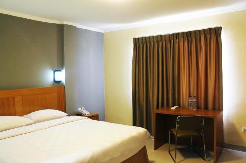 a bedroom with a bed and a desk with a chair at Maleosan Inn Manado Hotel in Manado