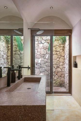 a bathroom with a large tub with a stone wall at 3BR Home in Gated Community with Private Rooftop Plunge Pool, Grill & Shared Pool in Tulum