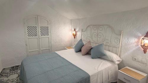 a white bedroom with a bed with blue and pink pillows at Cuevas Padre Poveda in Guadix