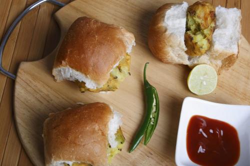 a cutting board with two sandwiches and a pickle at Hotel O Nirsukh Palace in Navi Mumbai