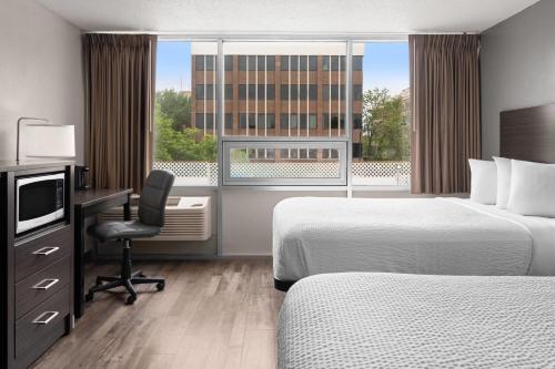 a hotel room with two beds and a desk and a window at Baymont by Wyndham Great Falls City Center in Great Falls