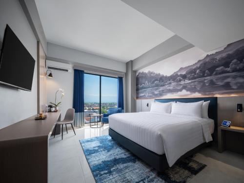 a hotel room with a bed and a desk and a large window at Aston Inn Lumajang - East Java in Lumajang