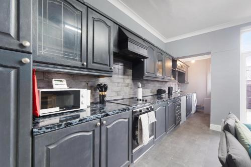 a kitchen with gray cabinets and a microwave at 4BR Mitchell Street Apartment Sleeps 6 by Stay With Us in Shield Row