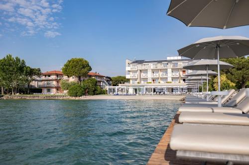 a row of lounge chairs with umbrellas next to the water at Hotel Ocelle Thermae & Spa - Adults Only in Sirmione