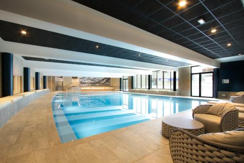 a large swimming pool in a hotel with chairs and tables at Hôtel et Spa l'Eclose by Odalys in L'Alpe-d'Huez