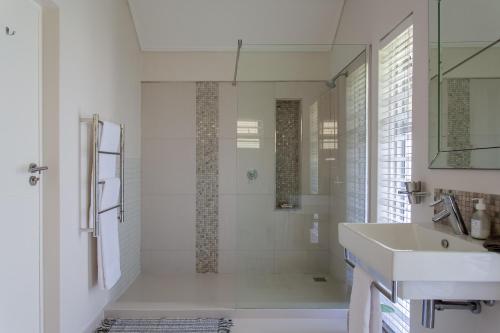 a white bathroom with a shower and a sink at The Barn Style Cottage in Cape Town