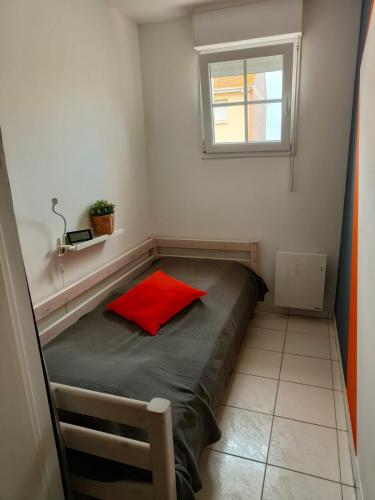 a small bed in a room with a red pillow at Vie de famille in Sainte-Cécile-Plage