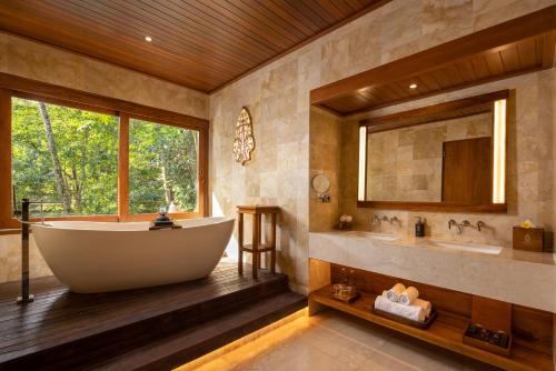 a bathroom with a tub and a sink and a mirror at The Kayon Resort in Ubud