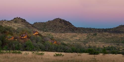 a house in a field with mountains in the background at Tshukudu Bush Lodge in Ledig