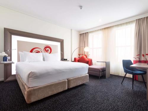 a hotel room with a large bed and a desk at Novotel Melbourne Glen Waverley in Glen Waverley