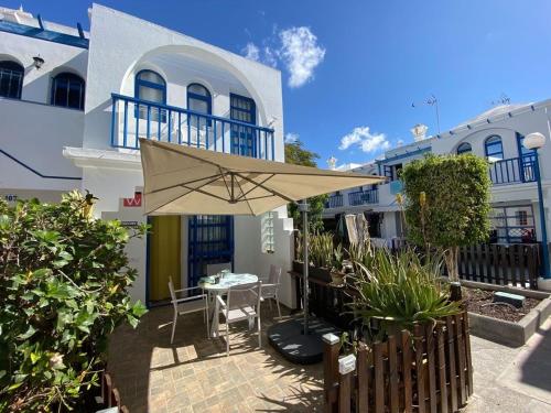 a patio with aige umbrella in front of a building at PLAYMAR Refugio Palmeras in Maspalomas