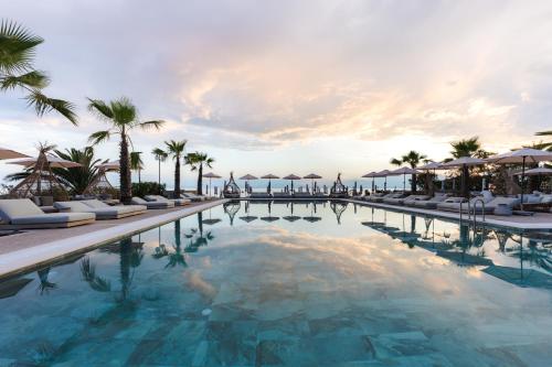 a pool at a resort with palm trees and umbrellas at Medite Kassandra Resort in Nea Moudania