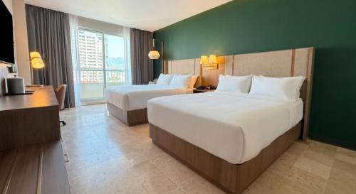a hotel room with two beds and a green wall at Holiday Inn Acapulco Amarea by IHG in Acapulco