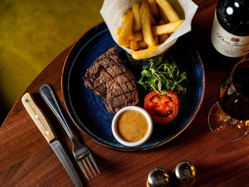 a blue plate with steak and french fries and a sauce at Mercure Haydock Hotel in Haydock