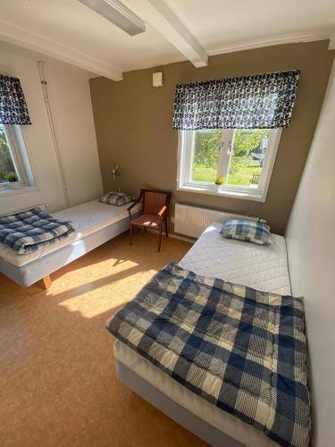 a bedroom with two beds and a chair and two windows at Norrfällsvikens Vandrarhem in Mjällom