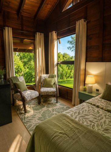 a bedroom with a bed and two chairs and a window at Refúgio Rural Ipê Lago e Fogueira ao Ar Livre in Campo Alegre