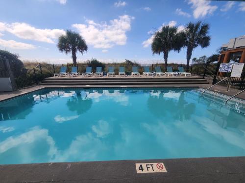 a large blue swimming pool with chairs and palm trees at Beachfront Bliss 3BR Oceanfront Condo with Pool and Hot Tub in Myrtle Beach