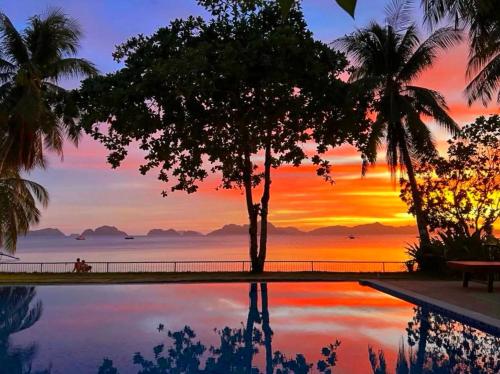 a pool with a tree and a sunset in the background at Doublegem Beach Resort and Hotel in El Nido