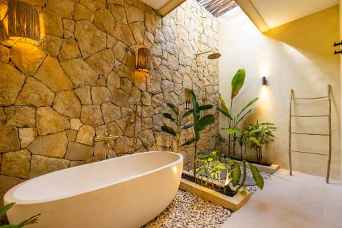 a bathroom with a bath tub and a stone wall at Uryah Hotel Lombok in Selong Belanak