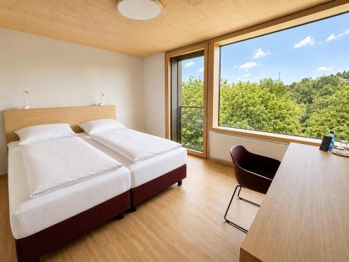 a bedroom with a bed and a desk and a large window at Tagungshotel Kloster Untermarchtal in Untermarchtal