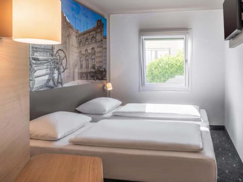 two beds in a room with a window at B&B HOTEL Düren in Düren - Eifel