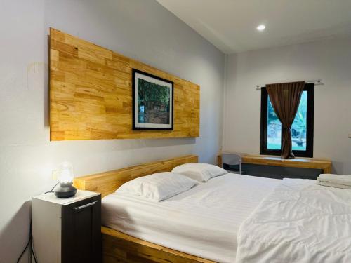 a bedroom with a white bed with a wooden headboard at บ้านไร่ดอกแก้ว in Chom Bung