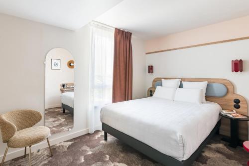 a bedroom with a bed and a chair and a window at Kyriad Lyon Est Stadium Eurexpo Meyzieu in Meyzieu