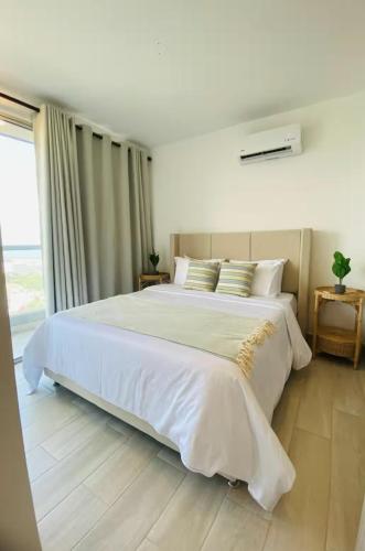 a large white bed in a bedroom with a window at Exclusivo apartasuite con terraza y vista al mar - Bello Horizonte in Santa Marta