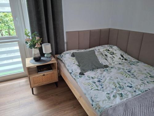 a bed in a bedroom with a vase on a night stand at Apartament VERDE Malbork centrum in Malbork