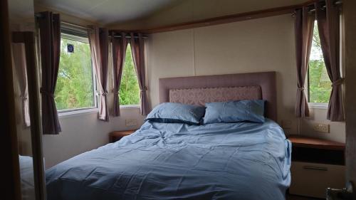 a bedroom with a bed with blue sheets and two windows at Sandpiper Aspen 9 in Peterhead