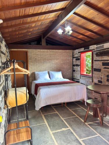 a bedroom with a bed and a table in a room at Chalé Carrara, um Refúgio de Pedra na Mata - Chalés Flor dos Manacás in Santa Teresa