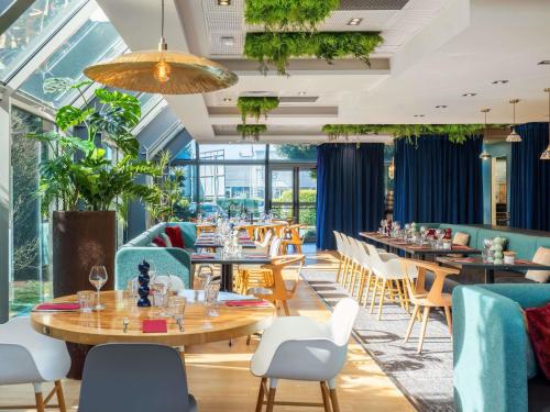 a restaurant with tables and chairs and windows at Novotel Lille Aéroport in Lesquin