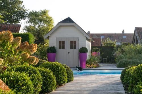 a small white shed next to a swimming pool at Country House Duinhof in De Haan