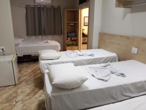 a room with three beds with white sheets at Hotel Rio Claro in Rio Claro