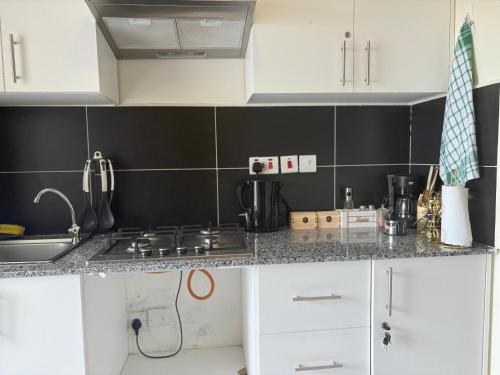 a kitchen with white cabinets and black tile walls at Luxore apartment in Syokimau