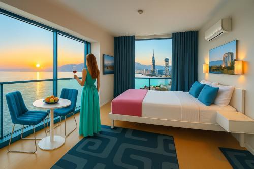 a woman standing in a hotel room with a bed and a window at Panorama Central Batumi in Batumi